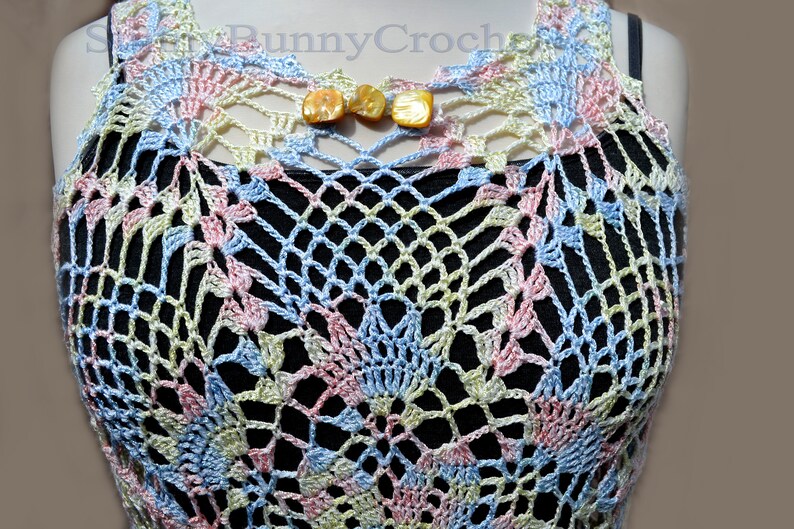 May include: A crocheted top in shades of blue, pink, and green. The top has a delicate, lacy pattern and is sleeveless. It features a small opening at the neckline with two decorative buttons.
