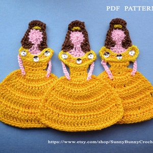 May include: Three crocheted Belle dolls from the Disney movie Beauty and the Beast. Each doll is wearing a yellow dress with a pink sash and brown hair. The dolls are arranged in a row on a blue background. PDF PATTERN
