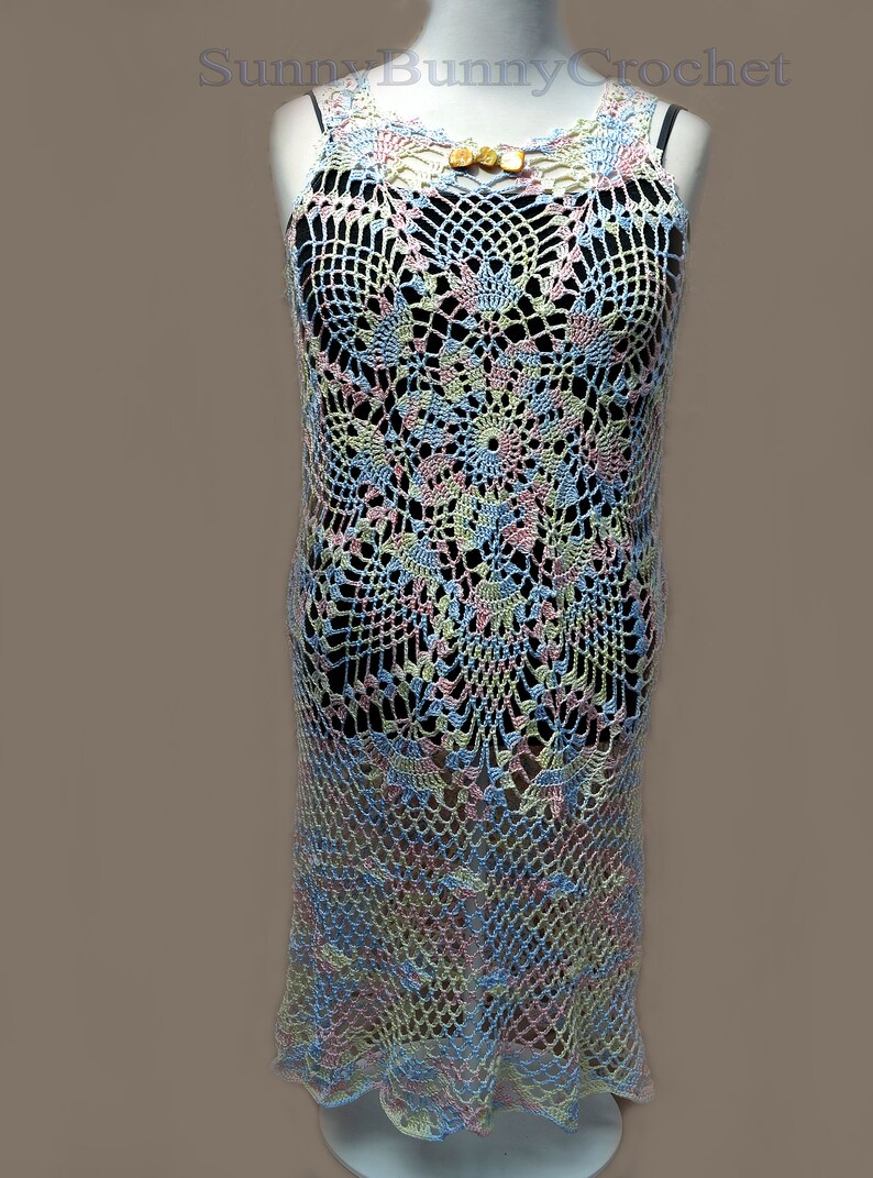 May include: A crocheted dress with a floral pattern in shades of blue, pink, and yellow. The dress has a sleeveless design and a scalloped hem.