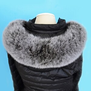 K&ouml;nnte beinhalten: Schwarze Steppjacke mit einem gro&szlig;en, flauschigen grauen Pelzkragen. Die Jacke ist aus wasserabweisendem Material gefertigt und hat ein gestepptes Design.
