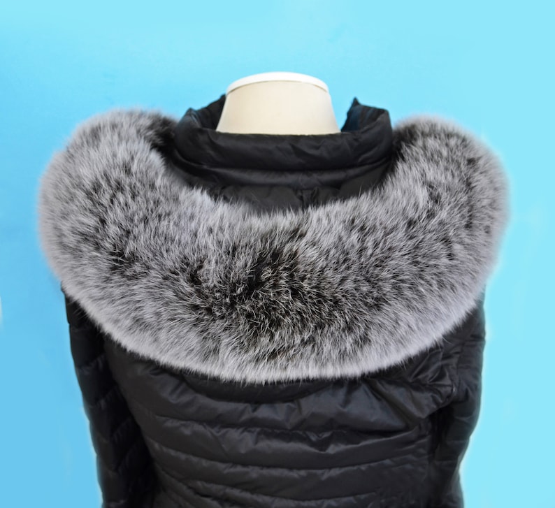 K&ouml;nnte beinhalten: Schwarze Steppjacke mit einem gro&szlig;en, flauschigen grauen Pelzkragen. Die Jacke ist aus wasserabweisendem Material gefertigt und hat ein gestepptes Design.