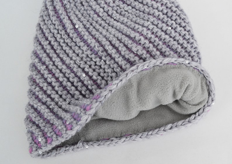 May include: Gray and purple knitted beanie with a fleece lining. The beanie has a diagonal pattern and is decorated with small silver sequins.