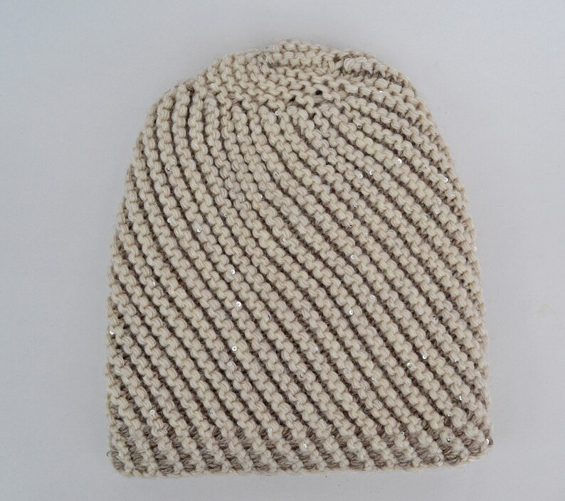 May include: A beige knitted beanie with a diagonal pattern and silver sequins.