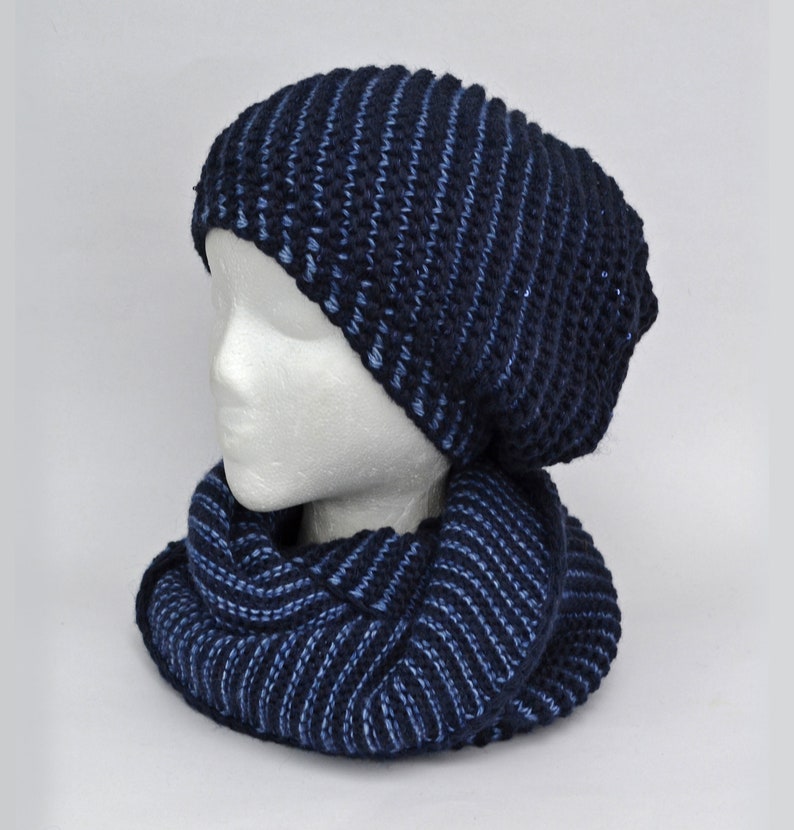 May include: A blue and dark blue striped knit hat and matching scarf set. The hat is slouchy and the scarf is a cowl style.