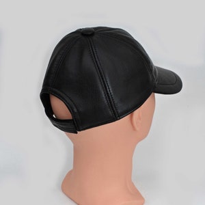 Puede incluir: Una gorra de b&eacute;isbol de cuero negro con visera curva. La gorra tiene un solo bot&oacute;n en la parte superior y un peque&ntilde;o agujero en la parte posterior.