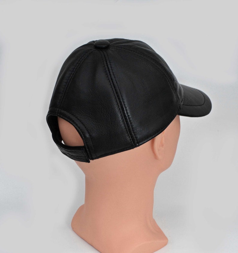 Puede incluir: Una gorra de b&eacute;isbol de cuero negro con visera curva. La gorra tiene un solo bot&oacute;n en la parte superior y un peque&ntilde;o agujero en la parte posterior.