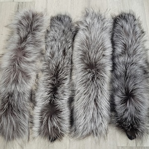 May include: Four silver fox fur tails, each with a long, fluffy texture. The tails are arranged in a row, with the tips of the tails pointing towards the right side of the image.