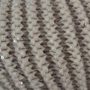 May include: Close-up of a knitted fabric with a striped pattern in beige and brown. The fabric is decorated with small silver sequins.