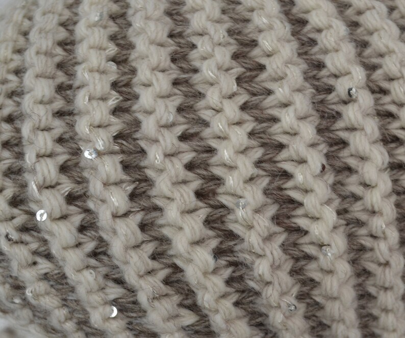 May include: Close-up of a knitted fabric with a striped pattern in beige and brown. The fabric is decorated with small silver sequins.