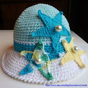 May include: A white crochet sun hat with a wide brim and three crocheted starfish embellishments. The starfish are in shades of blue, green, and yellow, and each has a pearl button in the centre.