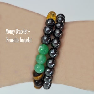 May include: Two beaded bracelets. One bracelet features a mix of green, yellow, and brown beads. The other bracelet is made of black beads. Text on the image reads "Money Bracelet + Hematite bracelet."