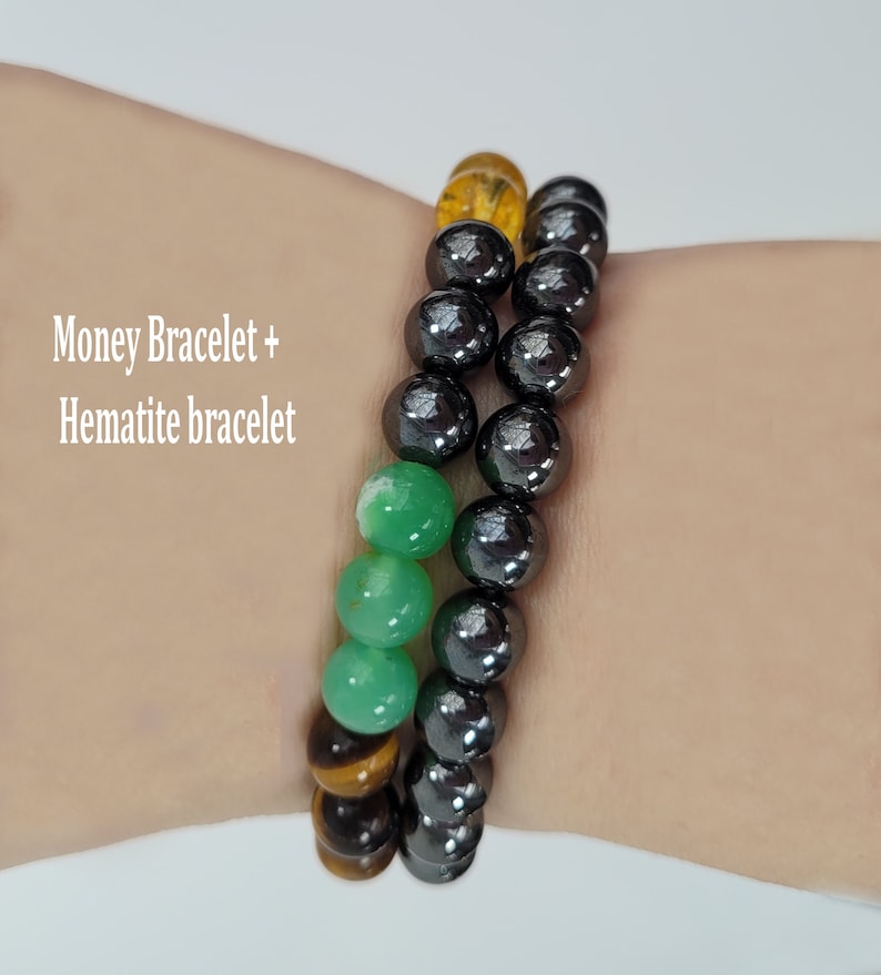 May include: Two beaded bracelets. One bracelet features a mix of green, yellow, and brown beads. The other bracelet is made of black beads. Text on the image reads "Money Bracelet + Hematite bracelet."