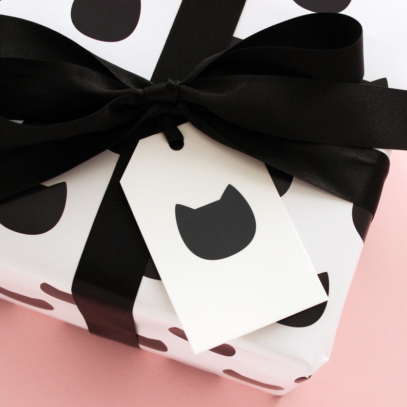 Traditional gift tag featuring a single black cat head attached to a gift with black ribbon wrapped in black cat wrapping paper.