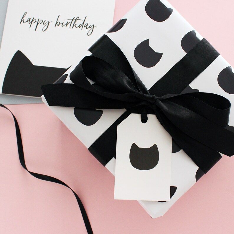 A gift wrapped in black cat wrapping with ribbon and a gift tag with a cat head.
