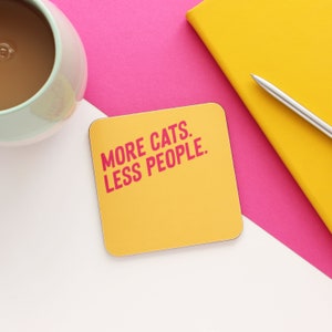 以下が含まれることがあります： ピンクの文字で「MORE CATS. LESS PEOPLE.」と書かれた黄色のコースターです。