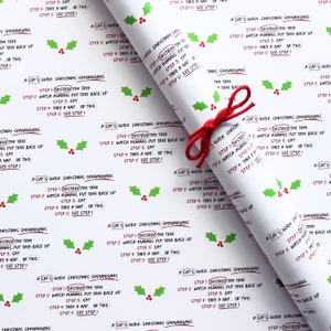 May include: White wrapping paper with a repeating pattern of green holly leaves and red berries. The paper features a festive message that reads "A Cat's Guide to Christmas Shenanigans" with a list of steps: "1. Destroy the tree, 2. Watch humans put tree back up, 3. Eat, 4. Take a nap, or two, 5. See step 1."