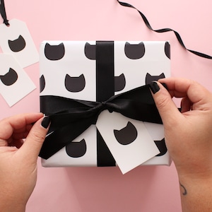 Hands tying a bow from black ribbon on a gift wrapped in black cat wrapping paper with a matching cat gift tag.