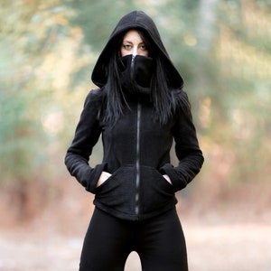 Puede incluir: Una chaqueta negra con capucha, cuello alto y cierre de cremallera. La chaqueta tiene un corte holgado y está hecha de un tejido suave y cómodo.