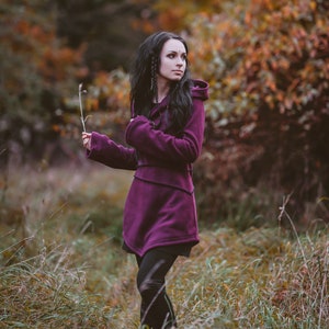 Peut inclure: Une femme portant un sweat &agrave; capuche violet se tient dans un champ d'herbe haute. Le sweat-shirt a un design long et fluide et est fait d'un tissu doux et confortable. La femme regarde de c&ocirc;t&eacute; et ses cheveux sont longs et fonc&eacute;s.