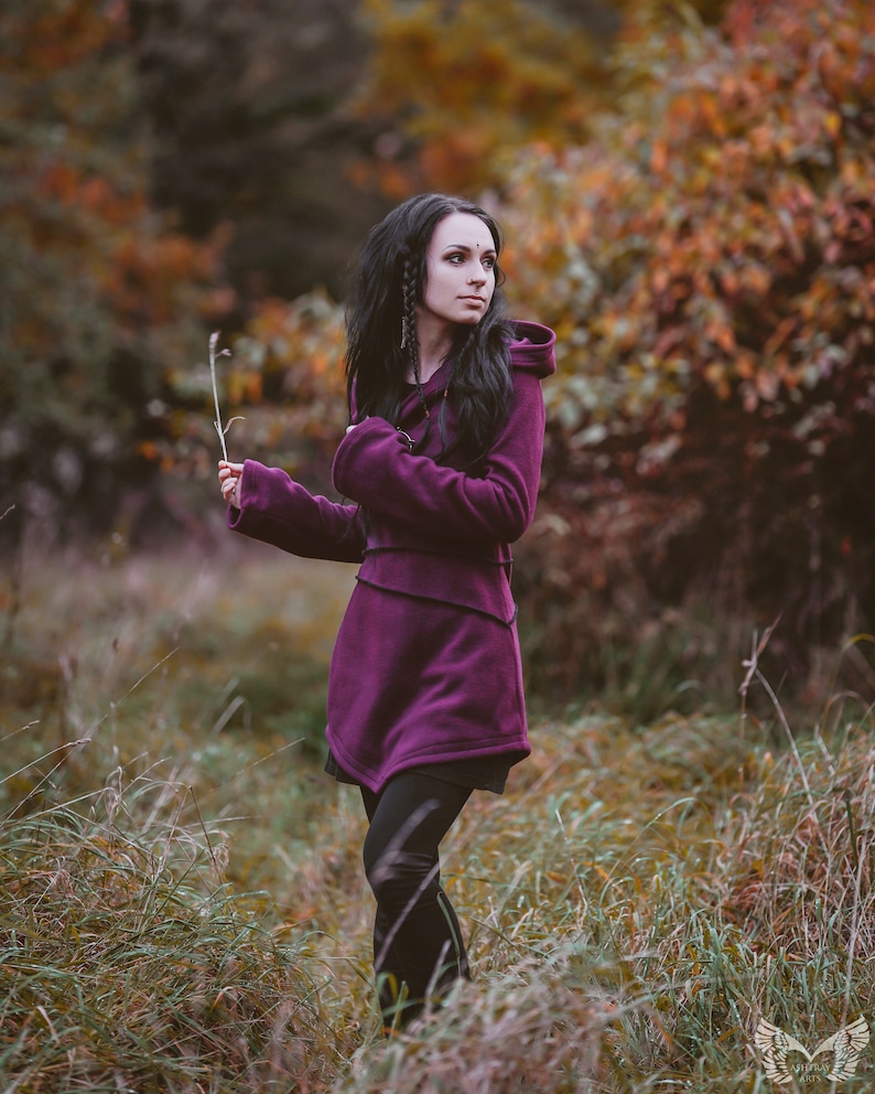 Peut inclure: Une femme portant un sweat &agrave; capuche violet se tient dans un champ d'herbe haute. Le sweat-shirt a un design long et fluide et est fait d'un tissu doux et confortable. La femme regarde de c&ocirc;t&eacute; et ses cheveux sont longs et fonc&eacute;s.