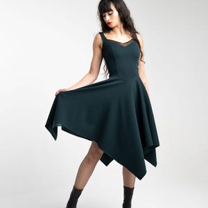 May include: A woman wearing a dark green asymmetric dress with a sweetheart neckline and black fishnet tights. She is wearing black ankle boots.