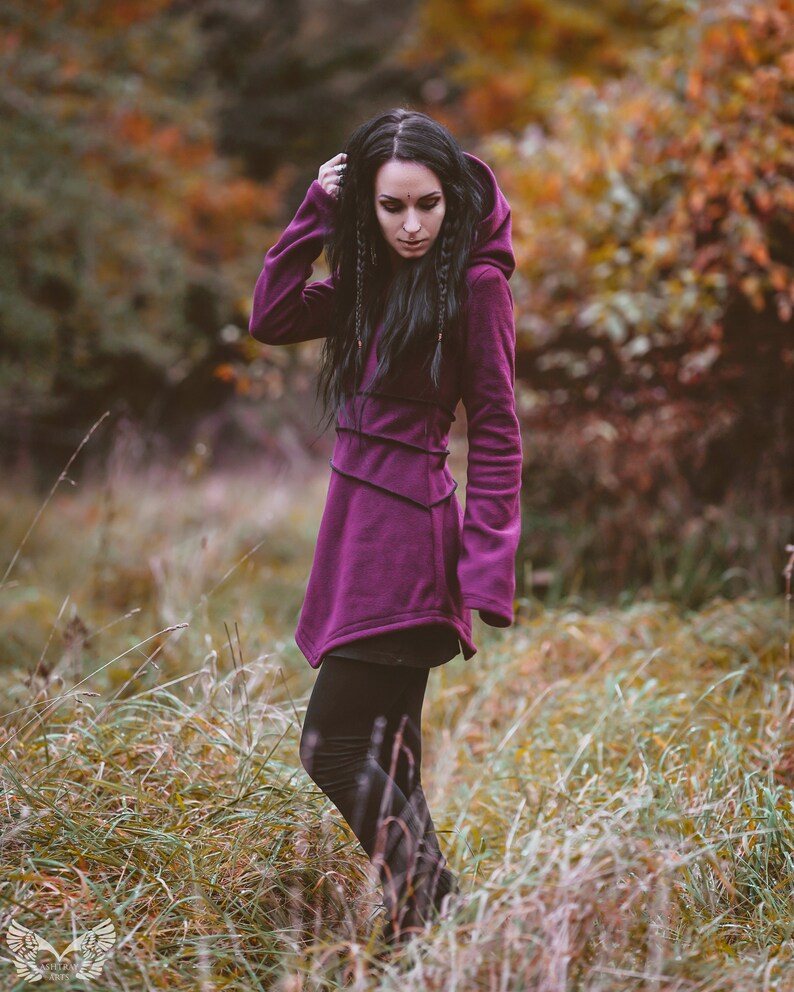 Peut inclure: Une femme portant un long sweat &agrave; capuche violet avec un legging noir. Elle se tient dans un champ d'herbe haute.