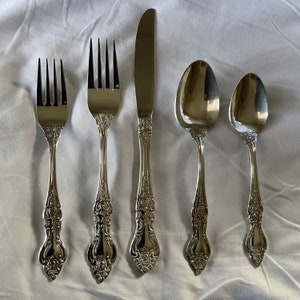May include: Five pieces of silverware, including a knife, two forks, and two spoons. The silverware is silver in color and has an ornate design.