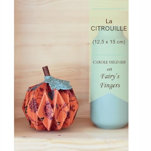 Puede incluir: Una calabaza de papel plegada con un patrón naranja y floral. La calabaza mide 12,5 cm por 15 cm. El título "La Citrouille" está escrito en texto marrón sobre un fondo amarillo. El texto "CARTONNAGE" está escrito en texto marrón sobre un fondo amarillo. El texto "CAROLE MEUNIER est Fairy's Fingers" está escrito en texto marrón sobre un fondo amarillo.