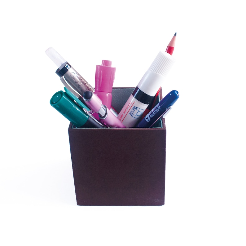 May include: A brown pencil holder with a pink highlighter, a green marker, a blue pen, a silver pen, and a red pencil inside.