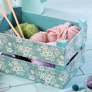 May include: A blue wooden crate with a floral pattern lining the inside. The crate is filled with balls of yarn in various shades of pink and green.