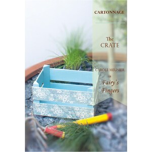 May include: A blue wooden crate with a white floral pattern. The crate is sitting on a gray stone surface. The text 'CARTONNAGE', 'The CRATE', 'CAROLE MEUNIER is Fairy's Fingers' is visible on the image.