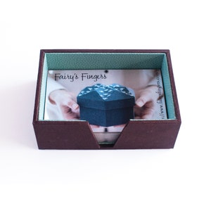 May include: A brown box with a green liner and a card inside. The card has a photo of a small, dark blue box with a white pattern on it. The text on the card reads 'Fairy's Fingers' and 'http://www.fairysfingers.com'. 