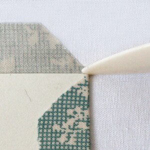May include: A close-up of a white fabric with a green and white fabric on top of it. A white tool is being used to press down on the fabric.