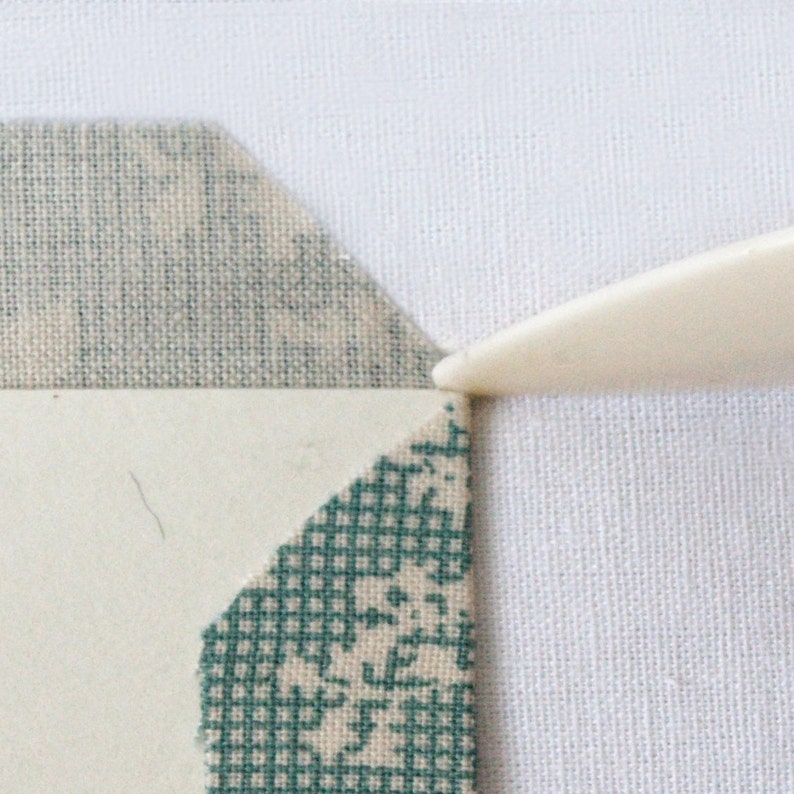 May include: A close-up of a white fabric with a green and white fabric on top of it. A white tool is being used to press down on the fabric.