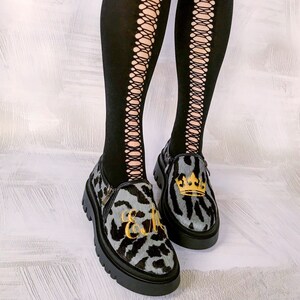 Könnte beinhalten: Ein Paar schwarze Netzstrümpfe mit einem Paar grau-schwarzen Leoparden-Schuhen. Die Schuhe haben eine goldene Krone und die Buchstaben "E & M" sind darauf gestickt.