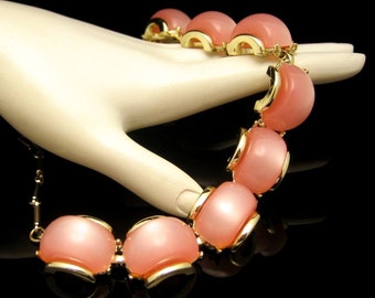 May include: A pink and gold statement necklace with large, round, opaque pink beads. The necklace is made of a chain with a gold clasp.