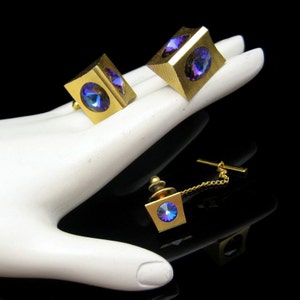May include: A set of three gold-toned cufflinks and a tie tack. Each piece features a square-shaped base with a large, iridescent purple gemstone in the center.