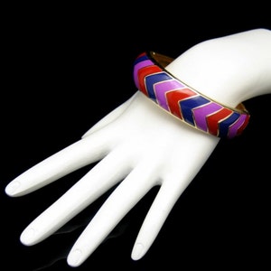 May include: A gold bangle bracelet with a chevron pattern in red, purple and blue enamel.