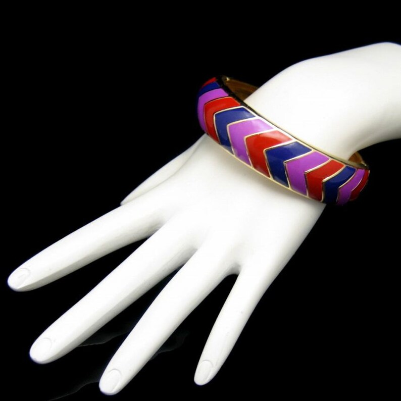 May include: A gold bangle bracelet with a chevron pattern in red, purple and blue enamel.