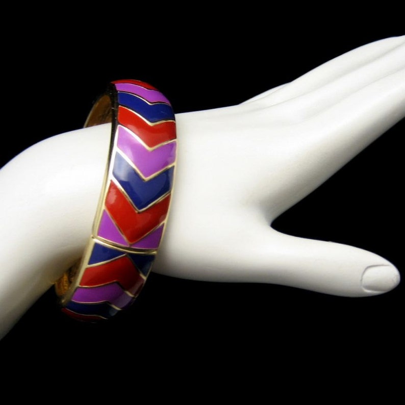May include: A gold bangle bracelet with a chevron pattern in red, purple and blue enamel.