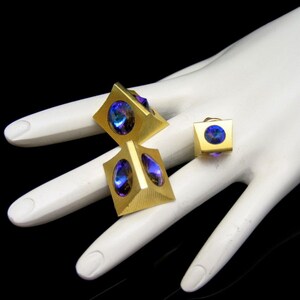 May include: A set of three gold-toned cufflinks with iridescent blue and purple stones. The cufflinks are shaped like pyramids with a square base.
