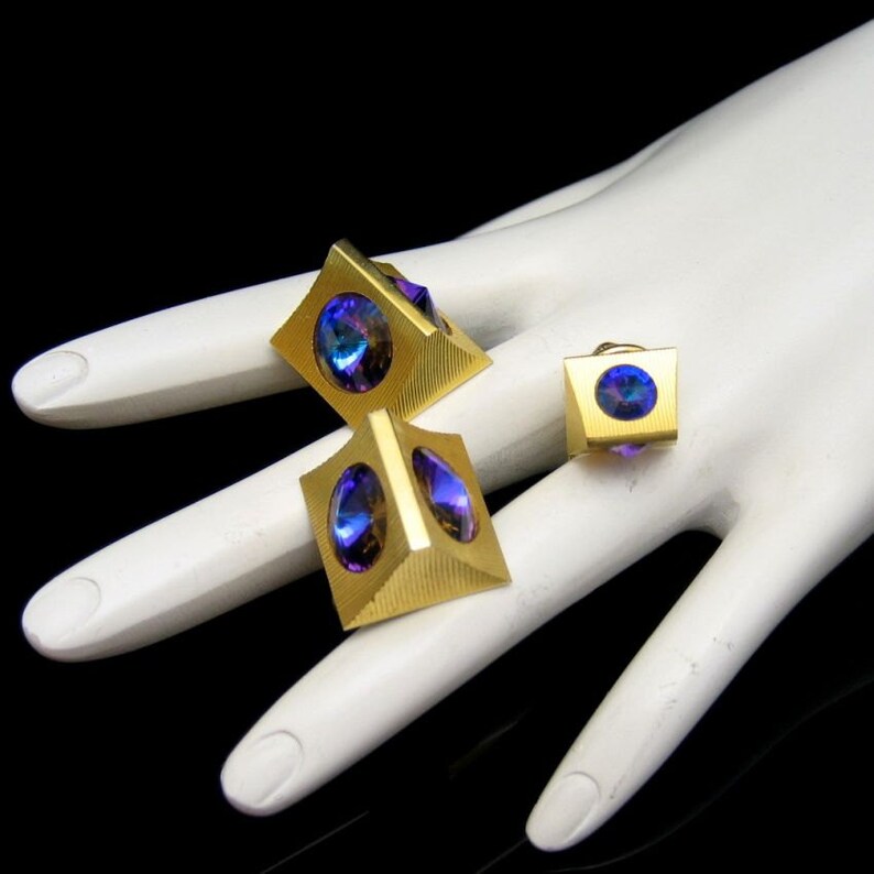 May include: A set of three gold-toned cufflinks with iridescent blue and purple stones. The cufflinks are shaped like pyramids with a square base.