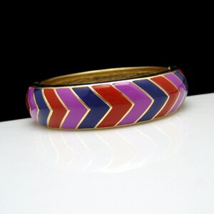 May include: A gold bangle bracelet with a chevron pattern in red, purple and blue enamel.