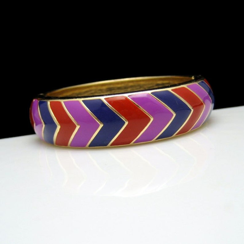 May include: A gold bangle bracelet with a chevron pattern in red, purple and blue enamel.