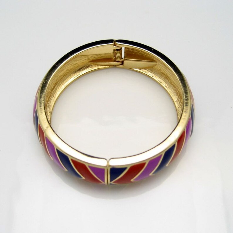 May include: A gold bangle bracelet with a geometric pattern in red, blue and purple enamel.