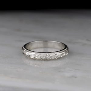May include: A simple silver wedding band with a delicate engraved design.