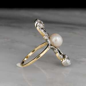 May include: A gold and silver ring featuring a large, round pearl as the centerpiece. The ring has a unique design with diamond accents on the sides. The band is gold, and the setting is silver.