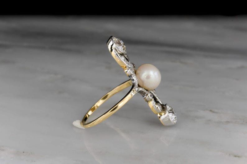 May include: A gold and silver ring featuring a large, round pearl as the centerpiece. The ring has a unique design with diamond accents on the sides. The band is gold, and the setting is silver.