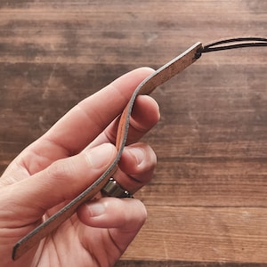 May include: A brown leather bookmark with a frayed edge and a knotted loop at the top.
