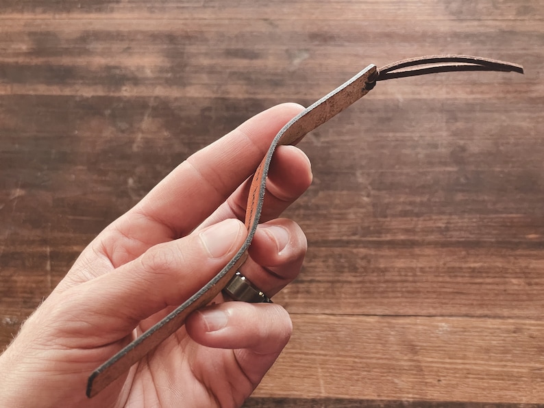 May include: A brown leather bookmark with a frayed edge and a knotted loop at the top.